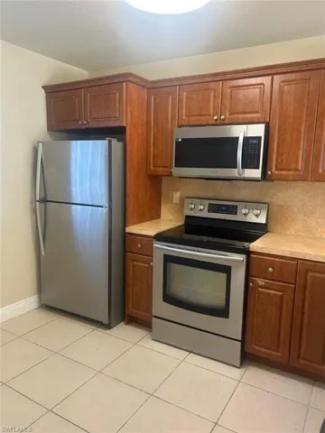 Kitchen with stainless steel appliances, light countertops, wood finish cabinets, and light tile patterned floors