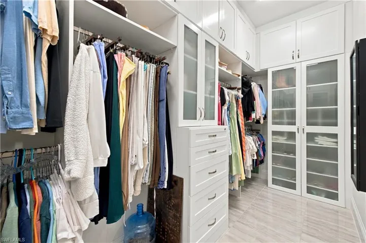 Custom dressing room featuring floor-to-ceiling white cabinetry, glass-fronted cabinet doors, integrated drawers with metallic hardware, and polished stone-finish flooring
