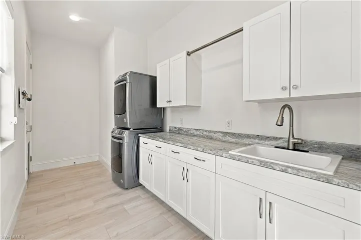 Laundry room featuring white shaker-style cabinetry, stone-patterned countertops, a drop-in sink with a gooseneck faucet, integrated hanging rod, and wood-finish flooring