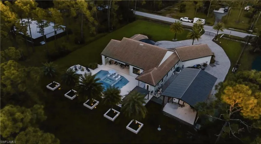 Aerial perspective of a sprawling residence featuring a tile roof, an integrated swimming pool with a spa, a detached covered structure, a paver driveway, and landscaped planters