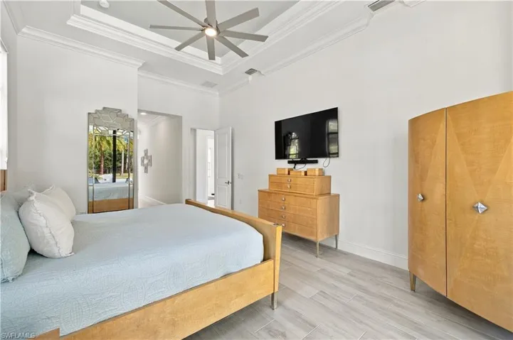 Tray ceiling with crown molding, multi-blade ceiling fan, and wood-finish flooring
