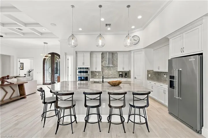 Kitchen featuring white cabinetry, stone-topped central island, stainless steel appliances, glass pendant lighting, and wood-finish flooring