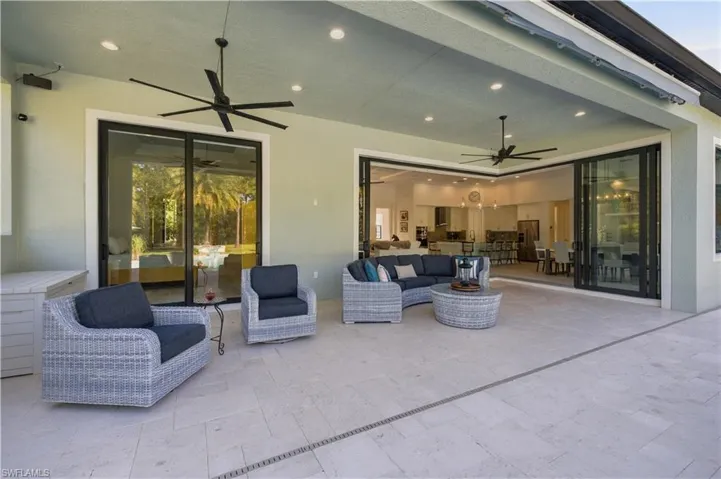 Covered patio featuring stone-tile flooring, dual ceiling fans, recessed lighting, and multi-panel sliding glass doors