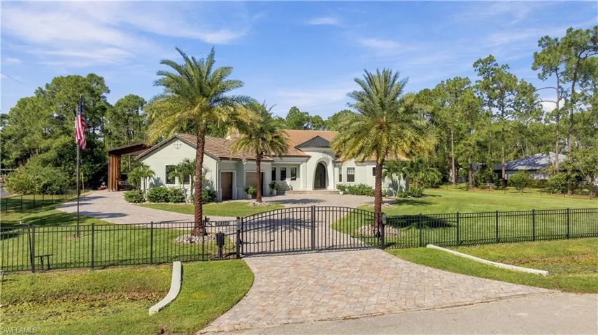 Stucco exterior featuring an arched entryway, gated brick-paver driveway, and mature landscaping