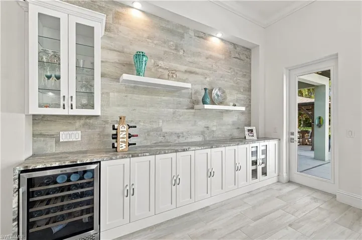 Custom built-in cabinetry featuring white shaker-style doors, stone-finish countertops, wood-finish wall accent, glass-front upper storage, and integrated beverage refrigeration