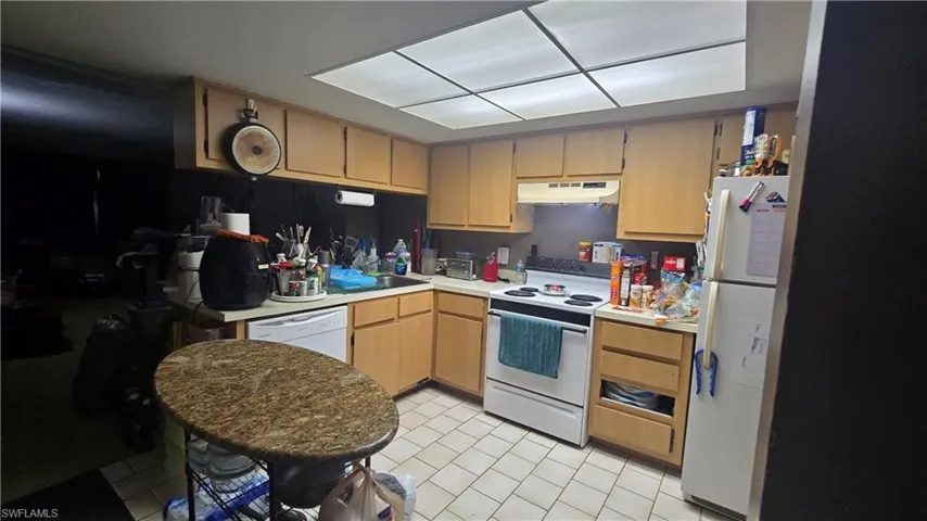 Kitchen with white appliances, light countertops, under cabinet range hood, and light tile patterned floors