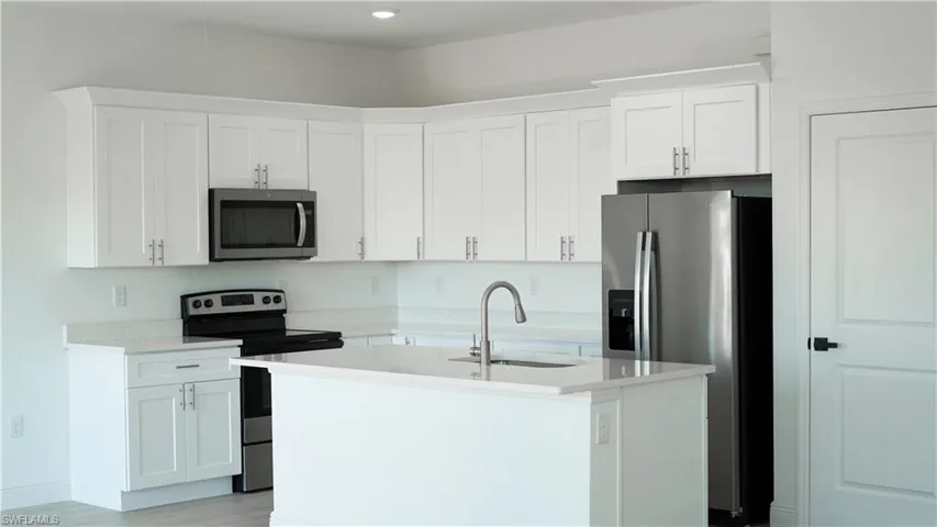Modern kitchen featuring white shaker cabinetry, stainless steel appliances, a center island with sink and gooseneck faucet, light-toned countertops, and recessed lighting