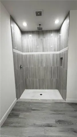 Walk-in shower featuring vertically laid gray-toned wall tiles with decorative horizontal stripe accents