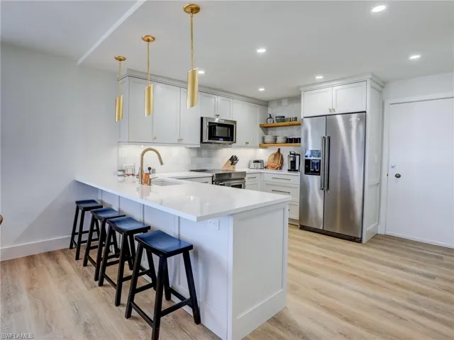 Kitchen with white cabinetry, light hardwood / wood-style flooring, stainless steel appliances, decorative light fixtures, and sink