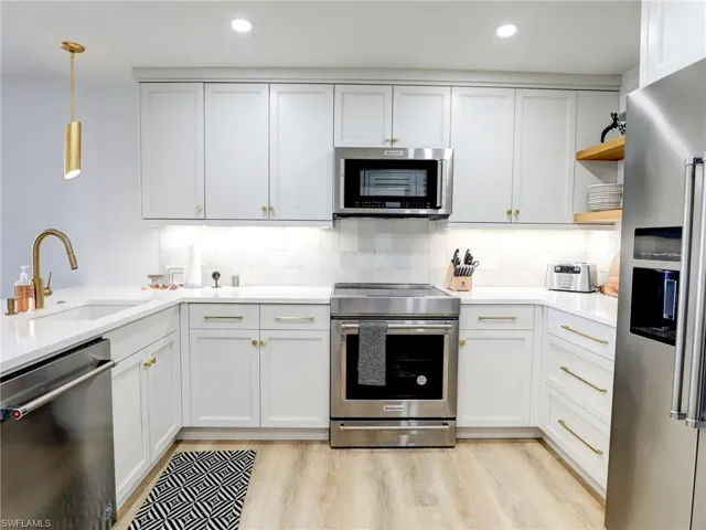 Kitchen with appliances with stainless steel finishes, tasteful backsplash, white cabinets, sink, and light wood-type flooring