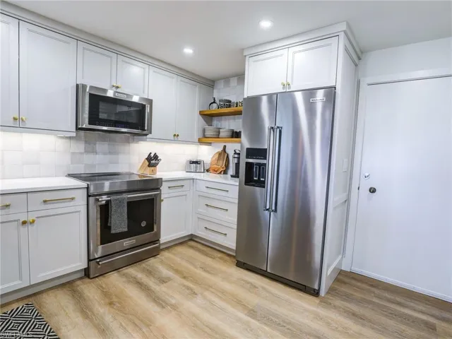 Kitchen with appliances with stainless steel finishes, white cabinetry, decorative backsplash, and light wood-type flooring