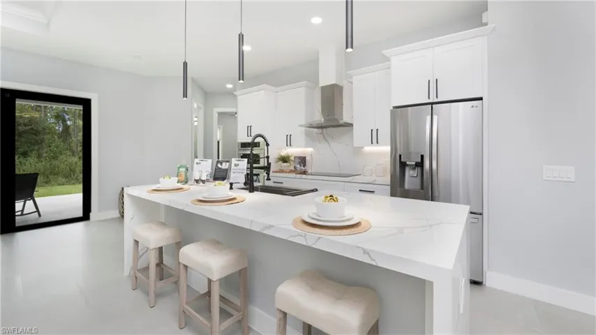 Kitchen with light stone countertops, stainless steel refrigerator with ice dispenser, a breakfast bar area, white cabinetry, and recessed lighting