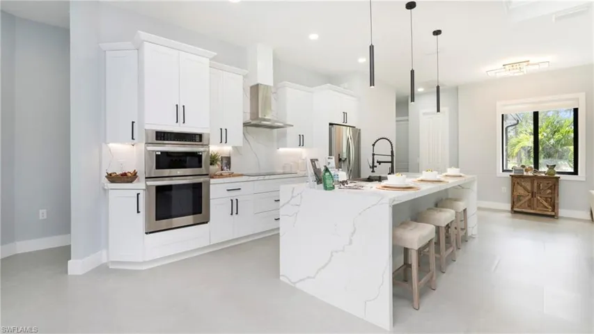 Kitchen featuring light stone counters, white cabinets, an island with sink, stainless steel appliances, and recessed lighting