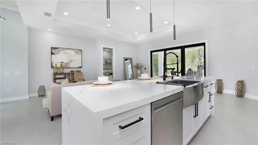 Kitchen featuring white cabinetry, a tray ceiling, stainless steel dishwasher, a center island with sink, and crown molding