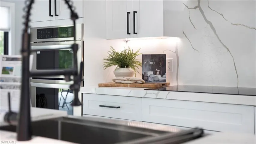 Kitchen view of white cabinets, stainless steel double oven, and black electric cooktop