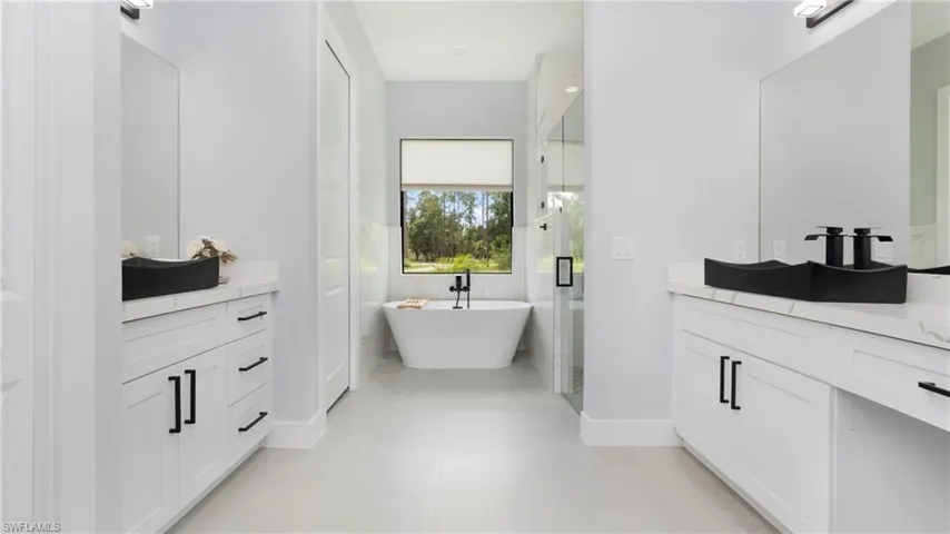 Bathroom featuring two vanities, a freestanding bath, a shower stall, and light tile patterned floors