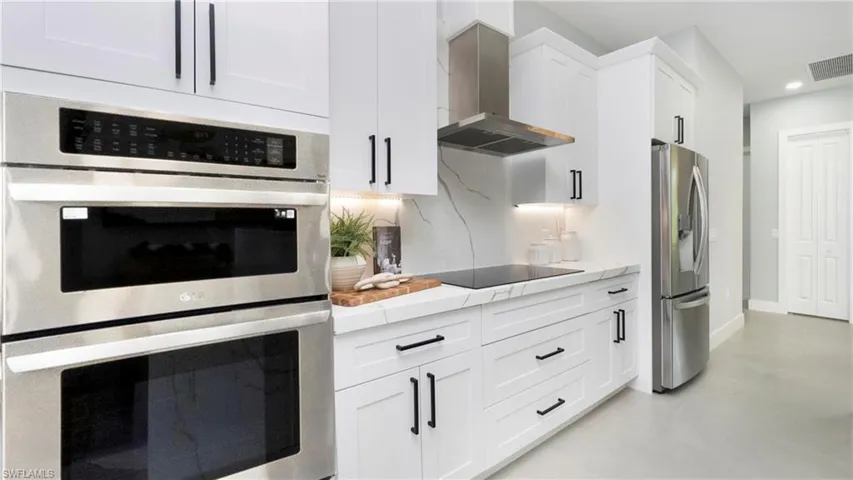 Kitchen featuring stainless steel appliances, wall chimney exhaust hood, white cabinetry, and recessed lighting