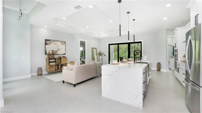 Kitchen with white cabinetry, freestanding refrigerator, decorative light fixtures, light stone counters, and a kitchen island with sink