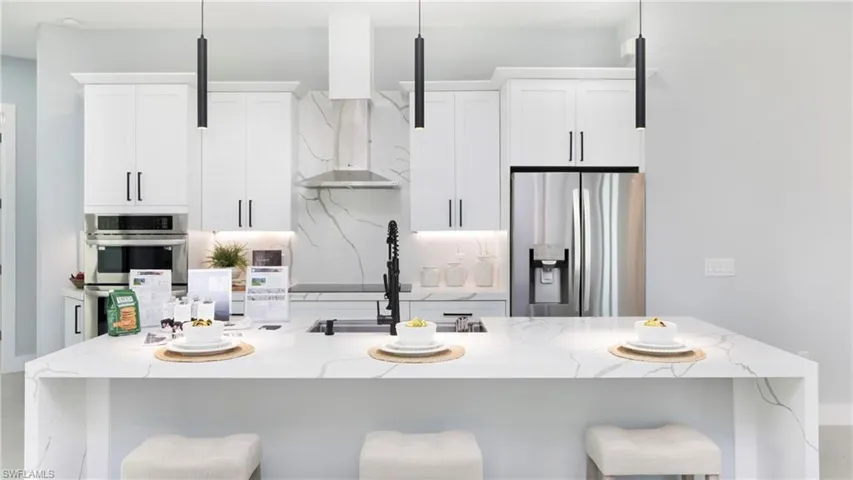 Kitchen featuring a breakfast bar area, light stone counters, an island with sink, and white cabinets