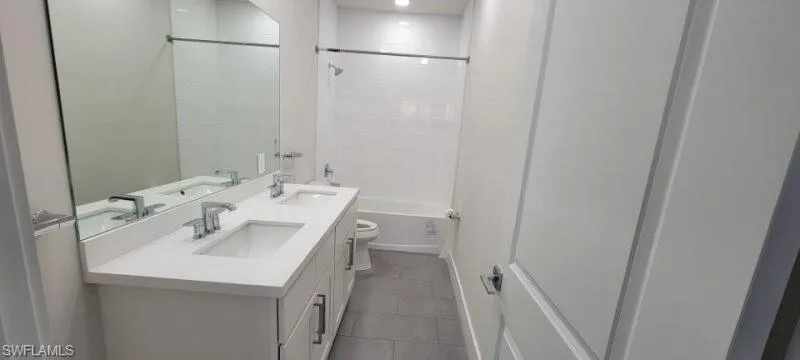 Full bath with toilet, double vanity, tile patterned floors, and bathing tub / shower combination