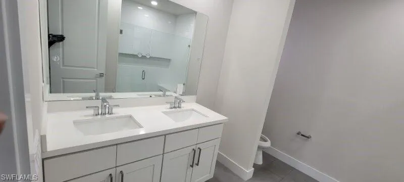 Bathroom featuring toilet, double vanity, baseboards, a stall shower, and tile patterned floors