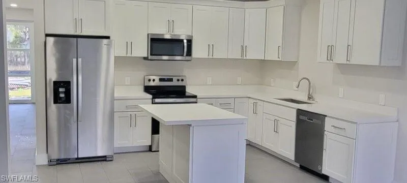 Kitchen with appliances with stainless steel finishes, a sink, a center island, white cabinetry, and light countertops