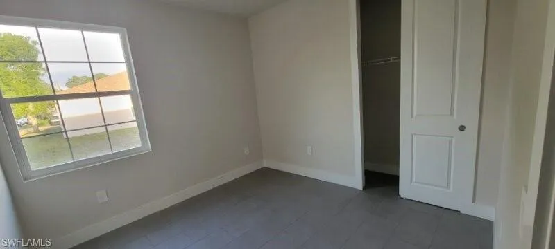 Unfurnished bedroom featuring baseboards, dark tile patterned flooring, and a closet