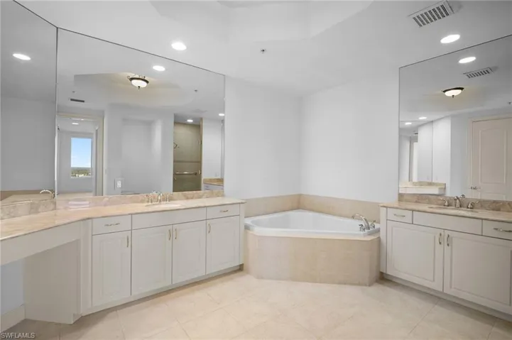 Bathroom with a tray ceiling, a shower stall, recessed lighting, two vanities, and a garden tub