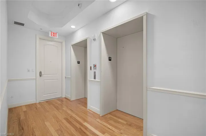 Hallway with elevator, light wood finished floors, a tray ceiling, crown molding, and recessed lighting