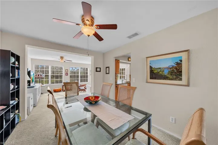 Carpeted dining area with a multi-blade ceiling fan and recessed lighting, featuring an open doorway to a sunroom with multiple grid-paned windows