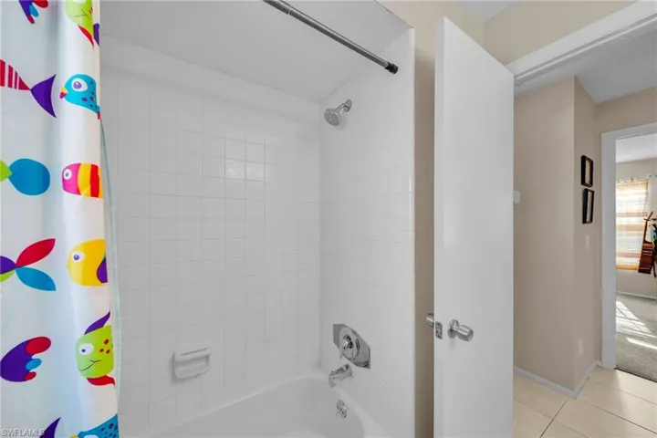 White tiled shower with a full bathtub, chrome fixtures, and a shower curtain rod