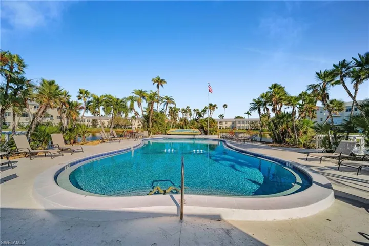 Community swimming pool with surrounding concrete deck, flanked by mature palm trees and residential buildings