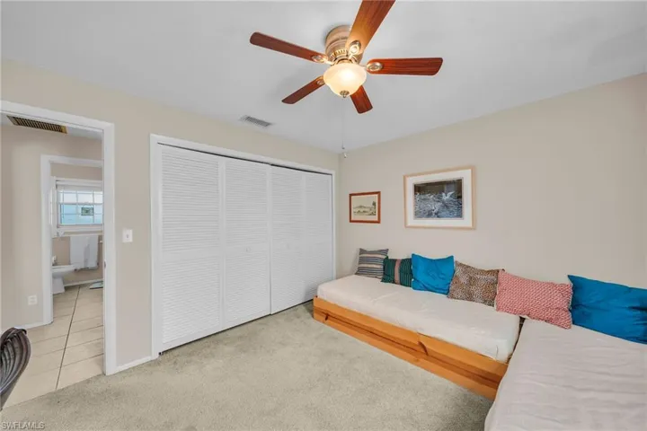 Room featuring textured carpeting, a ceiling fan with light fixture, and a built-in closet with louvered bi-fold doors