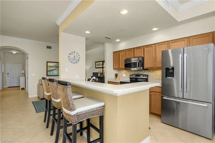 Kitchen with ornamental molding, appliances with stainless steel finishes, arched walkways, a breakfast bar area, and light tile patterned floors