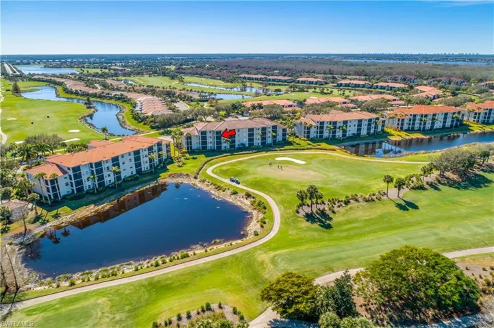 Drone / aerial view of the home with a red arrow pointing to the third floor unit, a golf course, and a large body of water