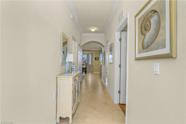 Hall featuring arched walkways, crown molding, and light tile patterned tile floors