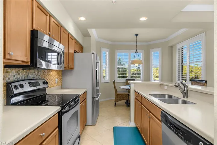 Kitchen featuring stainless steel appliances, hanging light fixtures, light tile patterned diagonal tile flooring, a bay window, and crown molding