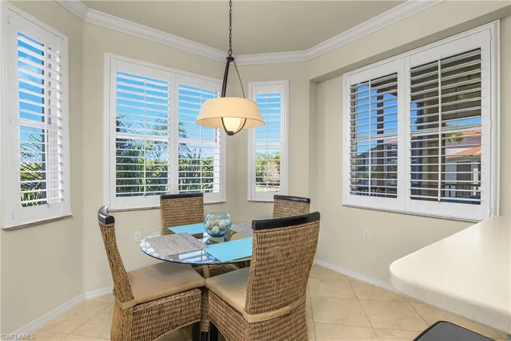 Dining area featuring light tile patterned flooring, crown molding, bay window with plantation shutters, and plenty of natural light