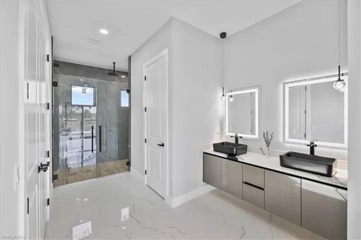 Full bathroom with double vanity, a marble finish shower, light marble finish flooring, and recessed lighting