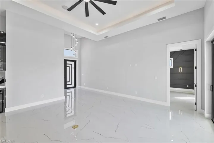 Unfurnished room featuring a raised ceiling, light marble finish floors, recessed lighting, and ceiling fan