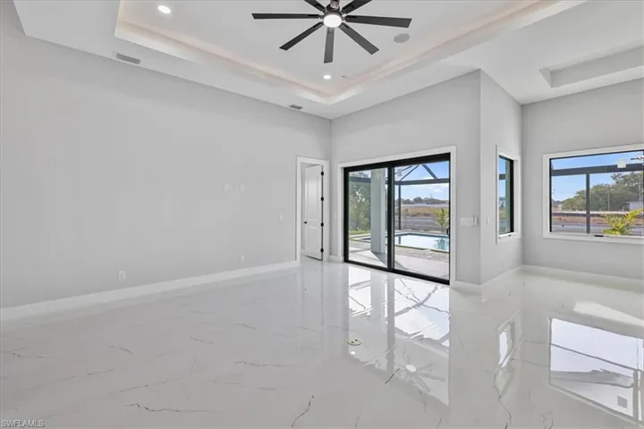 Unfurnished room featuring a tray ceiling, light marble finish flooring, a ceiling fan, and recessed lighting
