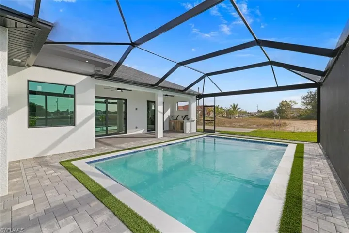 Outdoor pool featuring a sunroom, glass enclosure, a patio area, and an outdoor kitchen
