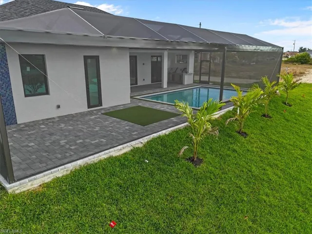 Rear view of house featuring glass enclosure, a patio area, a lawn, and an outdoor pool