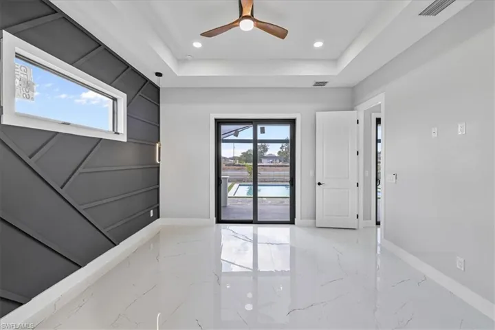 Spare room featuring a tray ceiling, a ceiling fan, light marble finish flooring, and recessed lighting