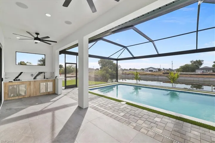 Swimming pool featuring exterior kitchen, a sunroom, glass enclosure, a patio, and a water view