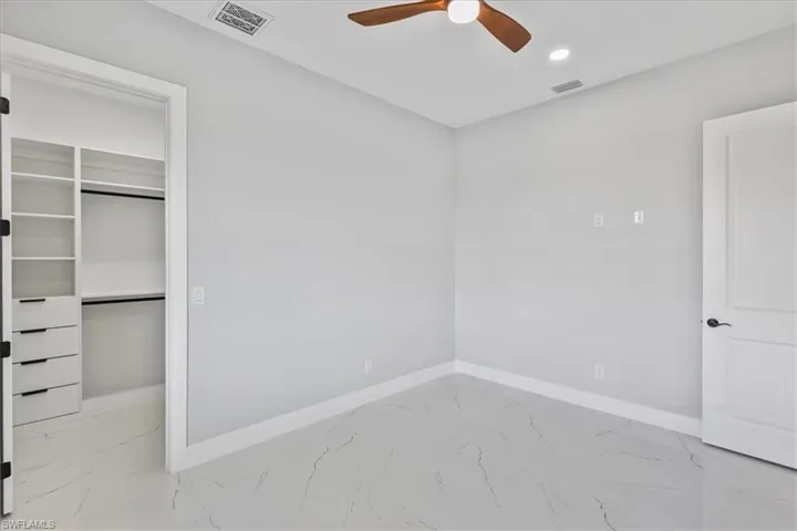 Unfurnished bedroom with a spacious closet, light marble finish flooring, a ceiling fan, and recessed lighting