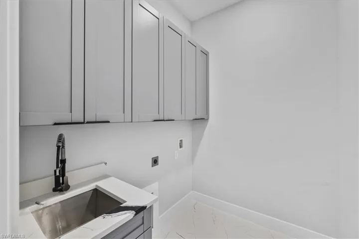 Washroom with hookup for an electric dryer, cabinet space, hookup for a washing machine, and light marble finish floors