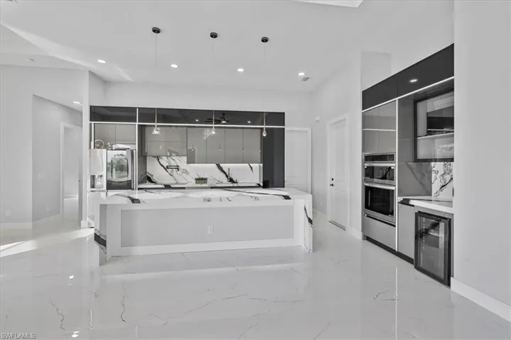 Kitchen with modern cabinets, light stone countertops, decorative light fixtures, beverage cooler, and recessed lighting