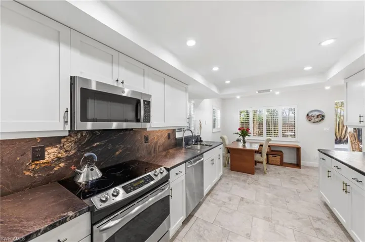 Kitchen with stainless steel appliances, a tray ceiling, white cabinetry, recessed lighting, and tasteful backsplash