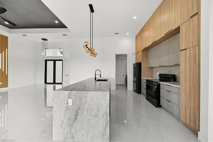 Kitchen with modern cabinets, black appliances, light stone counters, hanging light fixtures, and tasteful backsplash
